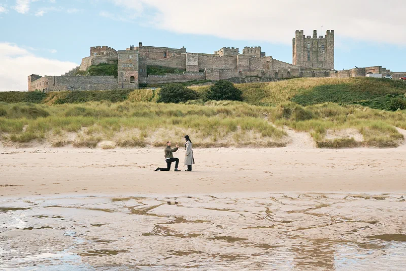 A man proposing on Bamburgh Beach with Bamburgh Castle above the dunes