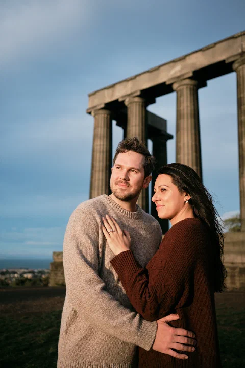 An engaged couple embracing in golden sunlight beside the columns on Calton Hill
